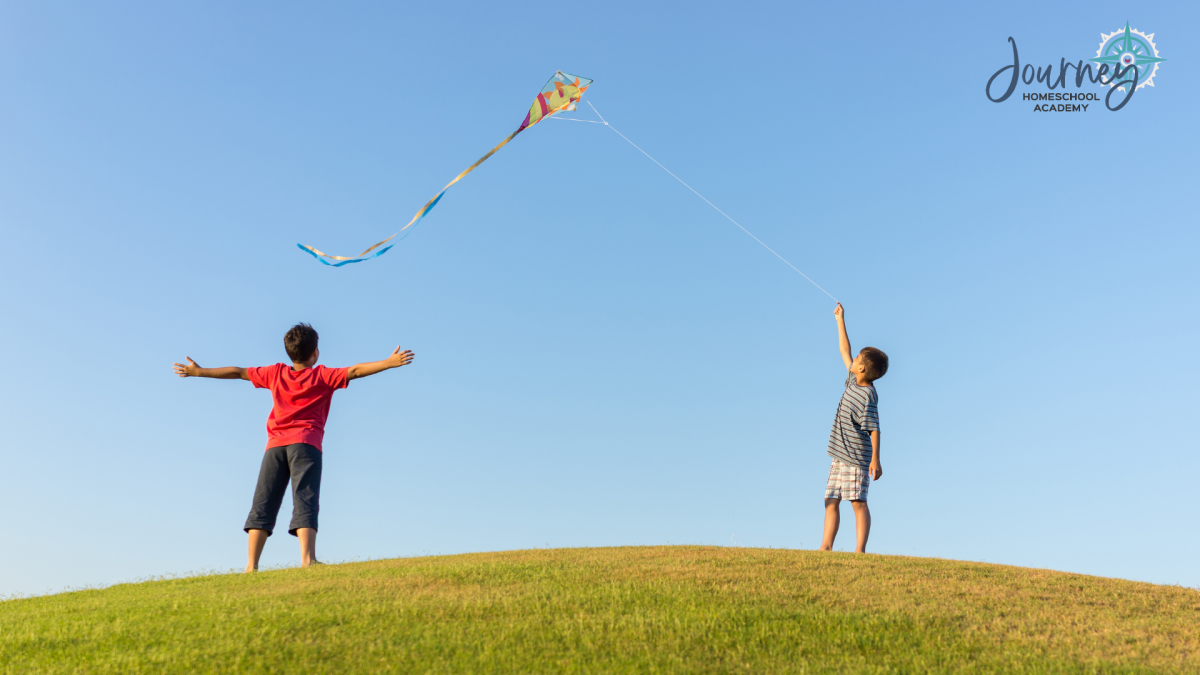 Two children flying a kite outdoors, a hands-on homeschool physics activity on lift and flight with Journey Homeschool Academy.