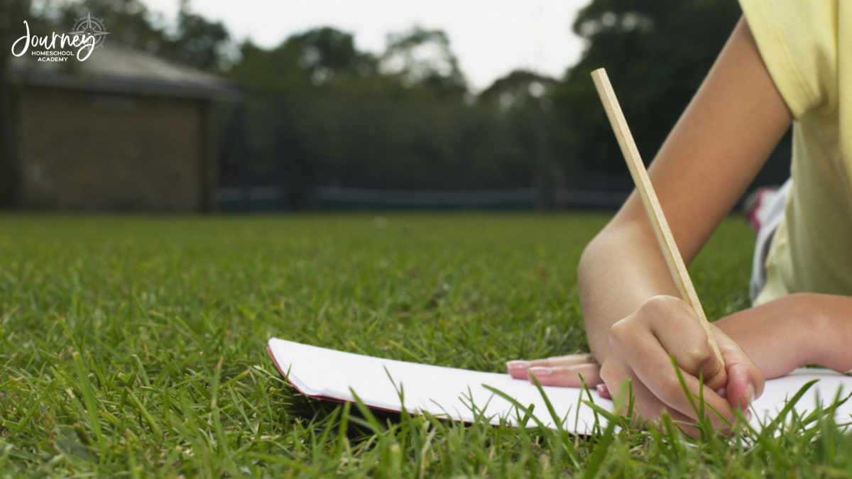 Child lying in the grass nature journaling in a homeschool backyard, connecting outdoor learning with bird friendly landscaping. Journey Homeschool Academy.