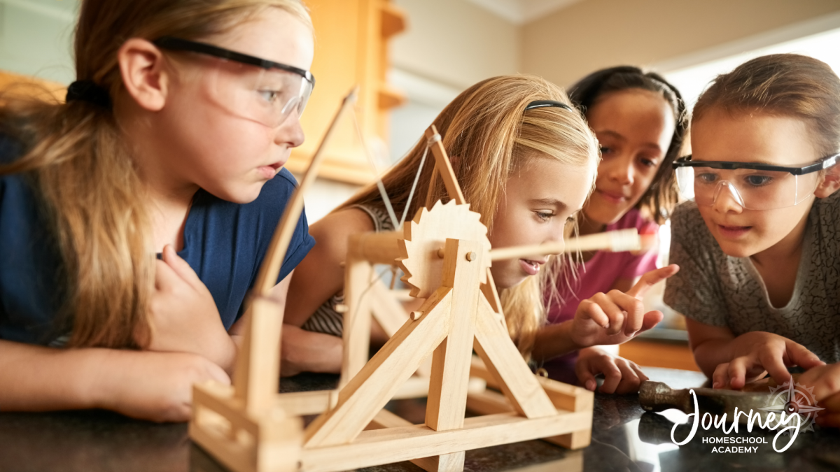 Group of children wearing safety goggles examining a small wooden catapult model during a homeschool science experiment, demonstrating hands-on learning.